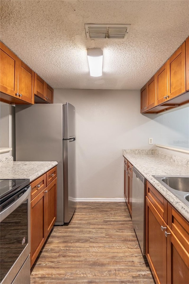 kitchen featuring stainless steel appliances, light stone countertops, a textured ceiling, and light hardwood / wood-style floors