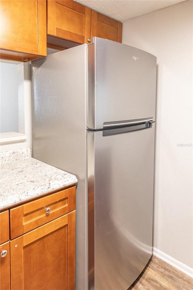 kitchen with stainless steel refrigerator, light stone countertops, a textured ceiling, and light hardwood / wood-style flooring