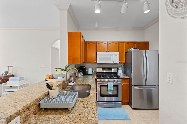 kitchen with light tile patterned floors, stainless steel appliances, a sink, ornamental molding, and brown cabinets