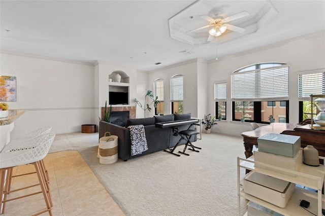 living room with a tray ceiling, crown molding, a fireplace, carpet flooring, and ceiling fan