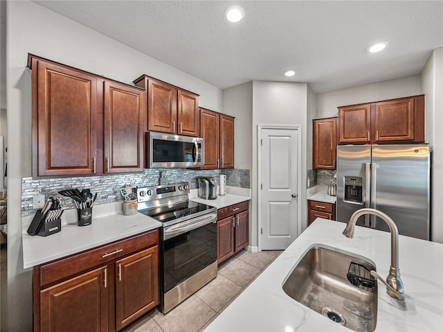 kitchen featuring light tile patterned flooring, sink, light stone counters, appliances with stainless steel finishes, and decorative backsplash