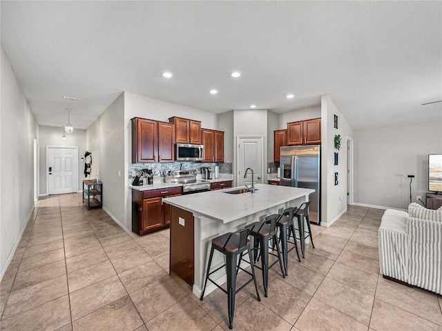 kitchen featuring sink, a breakfast bar, appliances with stainless steel finishes, tasteful backsplash, and a center island with sink