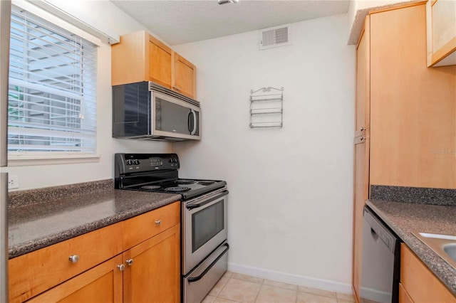 kitchen featuring appliances with stainless steel finishes, light tile patterned floors, and a textured ceiling