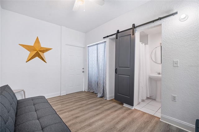 unfurnished living room featuring sink, a barn door, ceiling fan, and light wood-type flooring