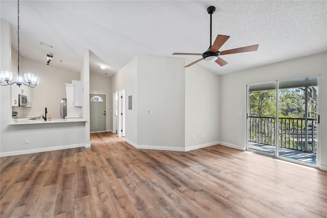 unfurnished living room with hardwood / wood-style flooring, vaulted ceiling, ceiling fan with notable chandelier, and a textured ceiling