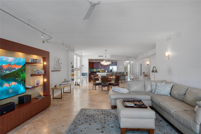 living room with ceiling fan with notable chandelier, rail lighting, and vaulted ceiling