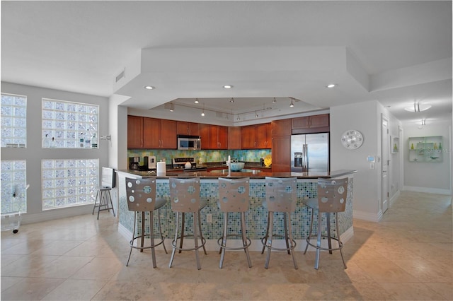 kitchen featuring tasteful backsplash, light tile patterned floors, stainless steel appliances, and a kitchen bar