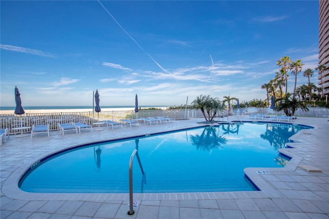 view of pool featuring a water view, a view of the beach, and a patio