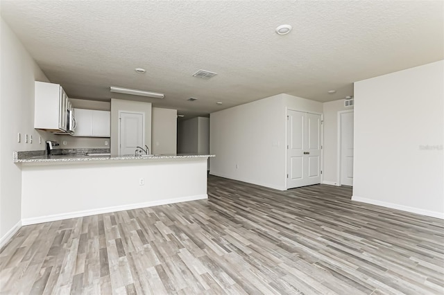 kitchen featuring a textured ceiling, kitchen peninsula, white cabinets, and light wood-type flooring