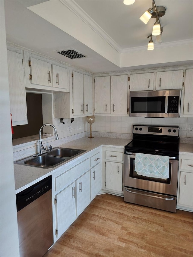 kitchen featuring sink, backsplash, ornamental molding, stainless steel appliances, and light wood-type flooring