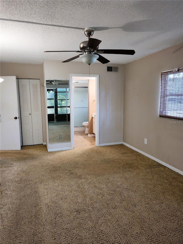 unfurnished bedroom featuring ceiling fan, ensuite bathroom, carpet flooring, and a textured ceiling