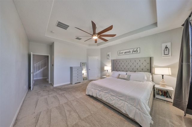 bedroom with a raised ceiling, light carpet, and ceiling fan