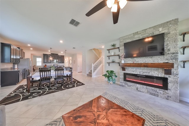 living room featuring light tile patterned floors, a stone fireplace, and ceiling fan