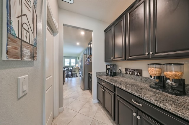 kitchen with dark stone countertops, stainless steel fridge, and light tile patterned floors