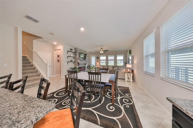 dining space featuring a large fireplace, ceiling fan, and light tile patterned flooring