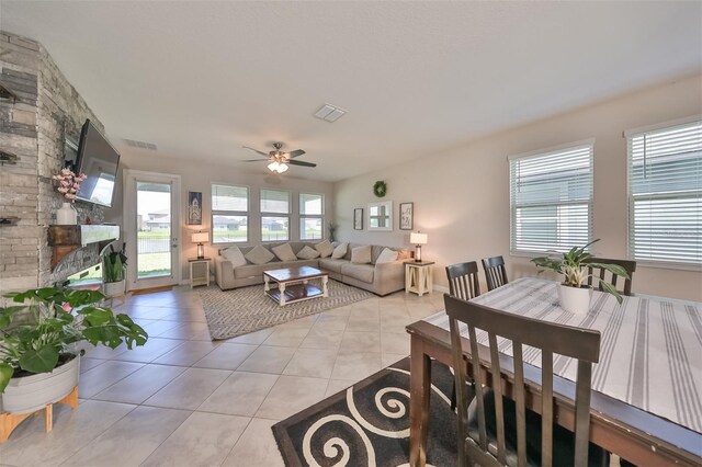 living room with light tile patterned floors, a stone fireplace, and ceiling fan