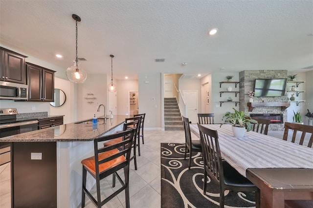 kitchen with sink, a kitchen island with sink, stainless steel appliances, a kitchen breakfast bar, and a stone fireplace