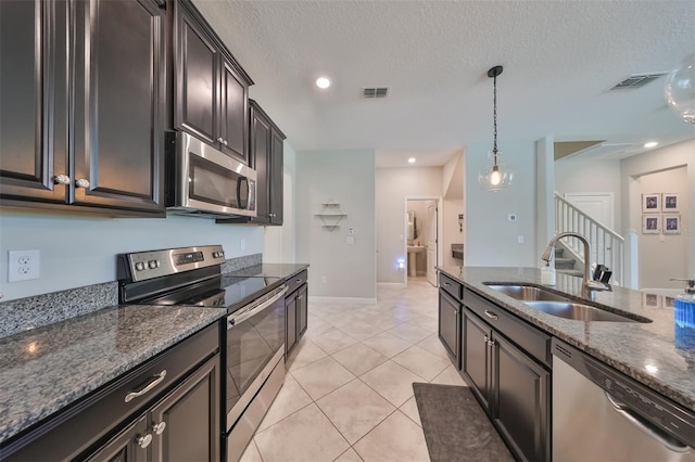 kitchen featuring pendant lighting, sink, stainless steel appliances, dark brown cabinetry, and dark stone counters