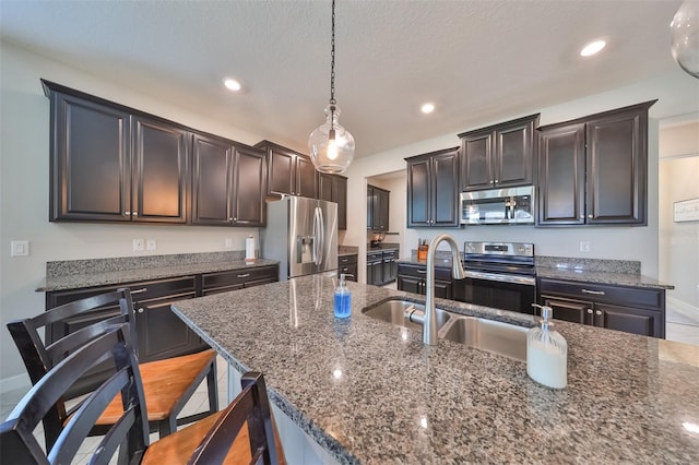 kitchen with sink, a breakfast bar area, stainless steel appliances, a center island with sink, and decorative light fixtures