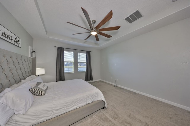 bedroom featuring a tray ceiling, light colored carpet, and ceiling fan