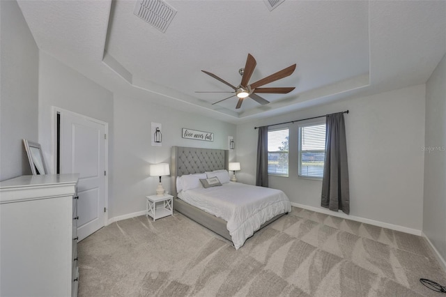 bedroom with ceiling fan, a tray ceiling, light carpet, and a textured ceiling