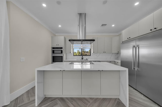 kitchen featuring tasteful backsplash, island range hood, ornamental molding, appliances with stainless steel finishes, and a center island