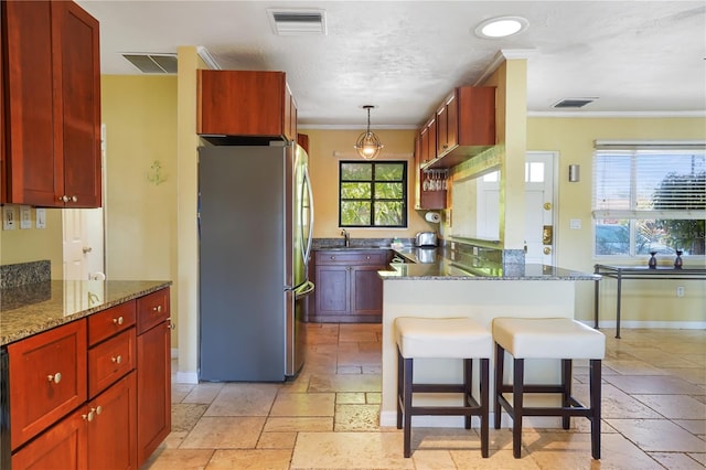 kitchen with pendant lighting, stainless steel refrigerator, dark stone countertops, a kitchen bar, and kitchen peninsula