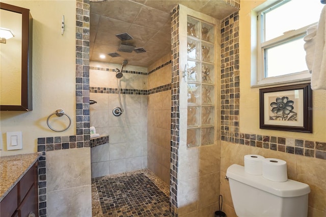 bathroom featuring vanity, tiled shower, tile walls, and toilet