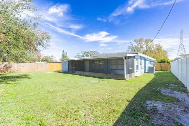 rear view of property with a sunroom, central AC, and a lawn