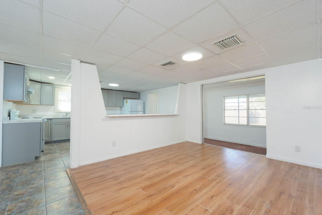 unfurnished living room with a drop ceiling, hardwood / wood-style floors, and plenty of natural light