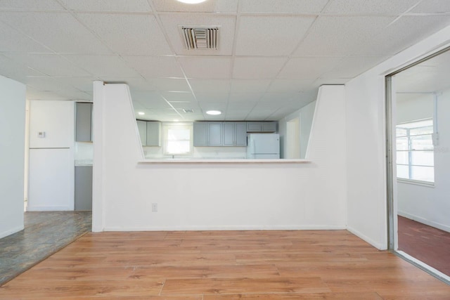 unfurnished living room featuring a drop ceiling, light hardwood / wood-style flooring, and a wealth of natural light