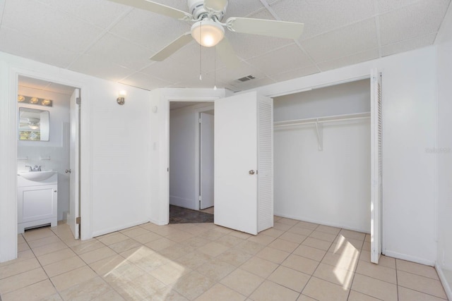 unfurnished bedroom with a paneled ceiling, sink, ceiling fan, ensuite bath, and a closet