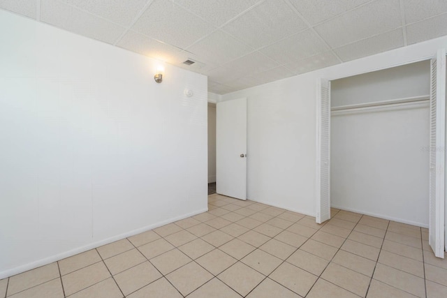 unfurnished bedroom with light tile patterned floors, a drop ceiling, and a closet