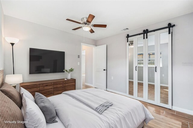 bedroom with ceiling fan, a barn door, and light wood-type flooring