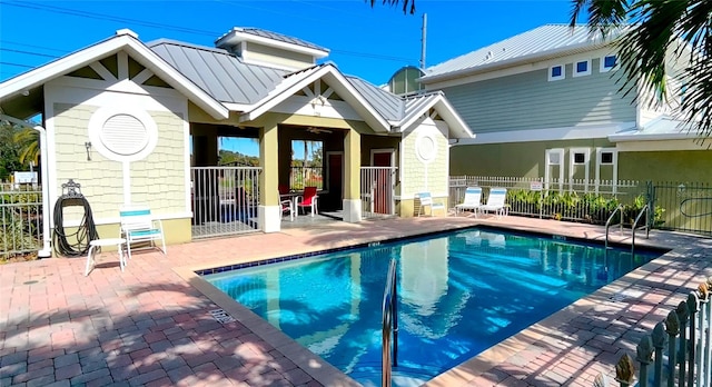 rear view of property with metal roof, a patio, a community pool, fence, and a standing seam roof