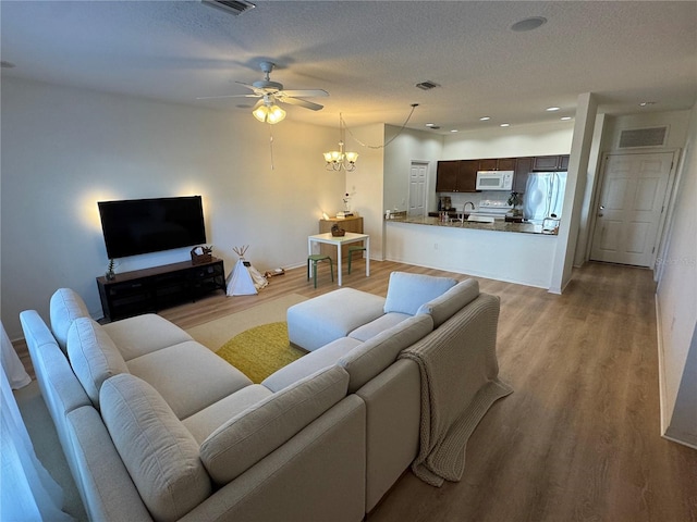 living room featuring light wood-type flooring, visible vents, a textured ceiling, and ceiling fan with notable chandelier