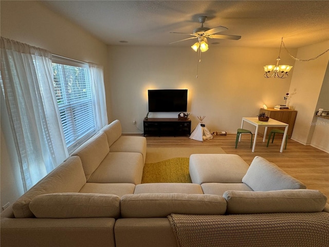 living room featuring ceiling fan with notable chandelier, baseboards, and wood finished floors