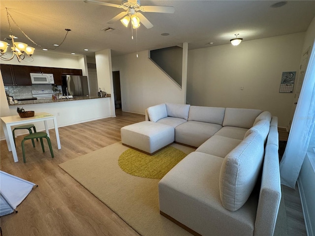 living room with light wood-style flooring, visible vents, and ceiling fan with notable chandelier