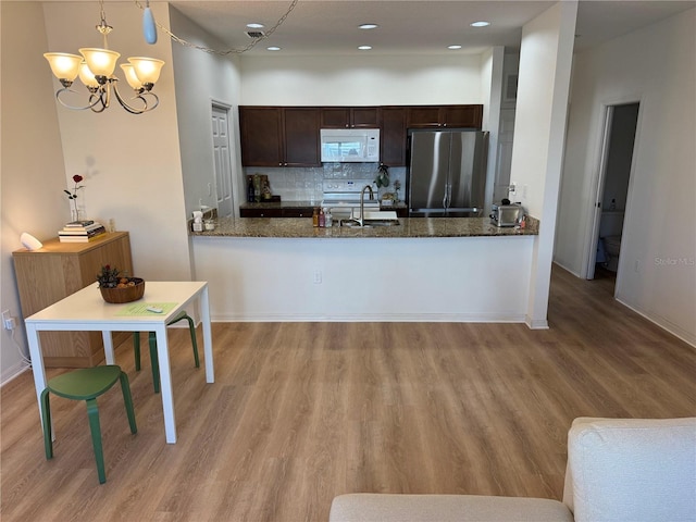 kitchen with white microwave, freestanding refrigerator, a sink, dark brown cabinetry, and a peninsula