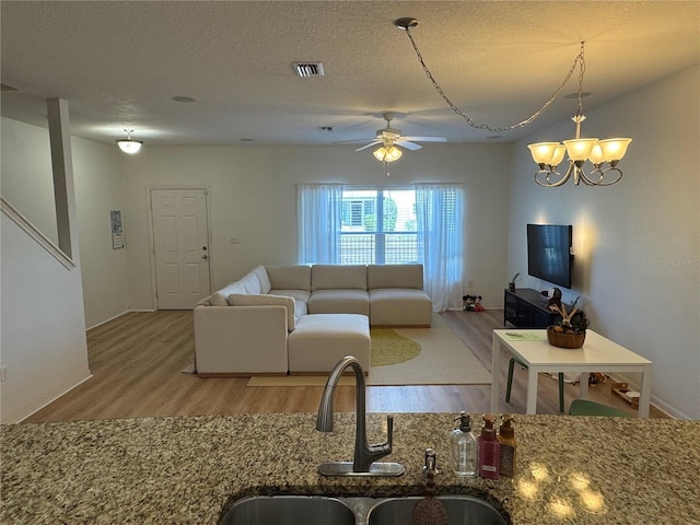 living room featuring ceiling fan with notable chandelier, visible vents, a textured ceiling, and wood finished floors