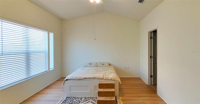 bedroom with light wood-type flooring, visible vents, baseboards, and vaulted ceiling