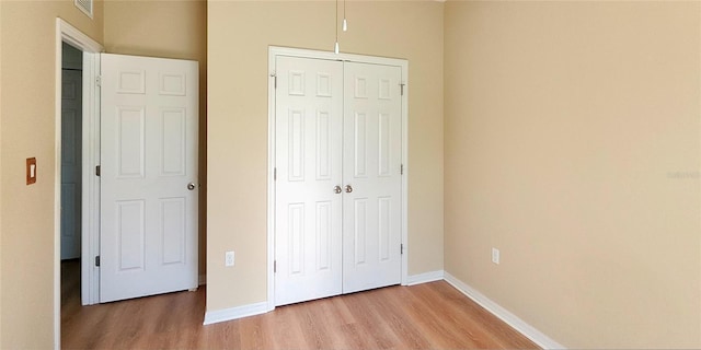 unfurnished bedroom featuring light wood-type flooring, a closet, visible vents, and baseboards