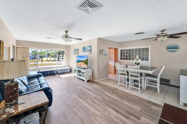 living room featuring ceiling fan, light hardwood / wood-style floors, and a textured ceiling