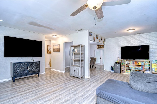 living room featuring light hardwood / wood-style flooring, ceiling fan, and brick wall