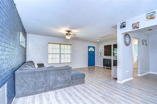 living room featuring wood-type flooring, ceiling fan, and brick wall