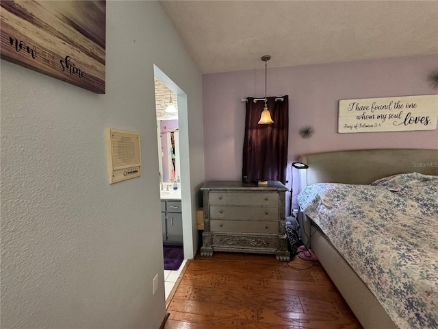bedroom featuring wood-type flooring, a textured wall, and connected bathroom