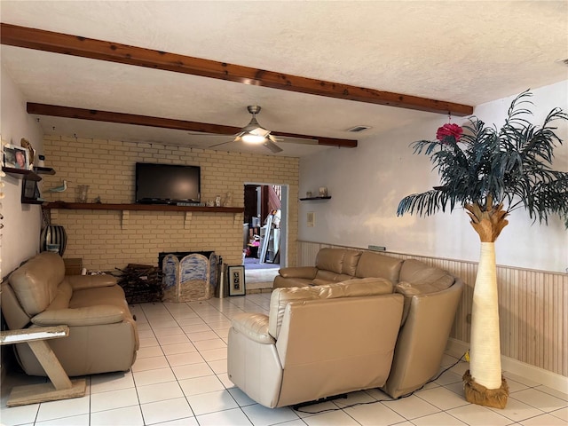 living room featuring light tile patterned floors, ceiling fan, a brick fireplace, beam ceiling, and visible vents