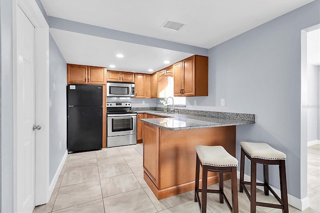 kitchen with sink, stainless steel appliances, kitchen peninsula, a kitchen bar, and dark stone counters