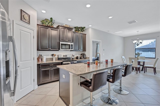 kitchen featuring a breakfast bar, light tile patterned floors, an island with sink, pendant lighting, and stainless steel appliances