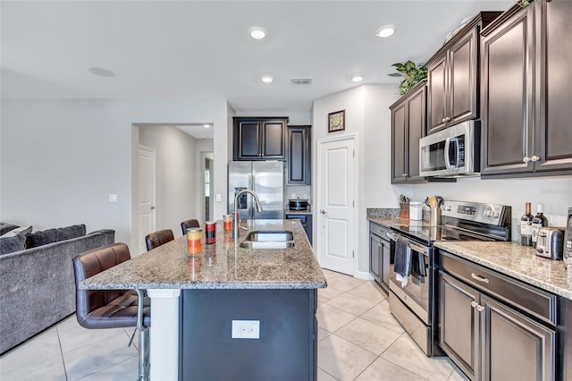 kitchen with a breakfast bar, sink, a kitchen island with sink, dark brown cabinetry, and stainless steel appliances